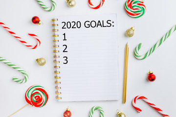 2020 goals plans dreams. New Year and Christmas, concept writing in notebook. Christmas balls, candy cane and notebook on white background, Christmas planning concept. Flat lay. Top view