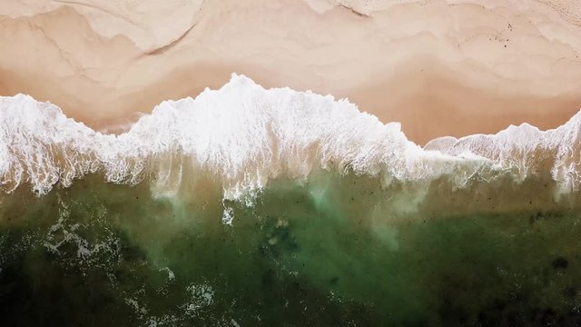 Aerial view on turquoise huge waves with white foam which covers empty beach. Top view from drone on sandy coast 