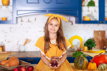 Little girl sitting on working surface of kitchen is waiting for breakfast with jar of jam....