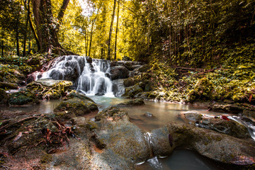 The natural background of waterfalls that blur the flow of water, with various tree species surrounded and boulders of various sizes, the beauty of the ecosystem and the jungles of forests.