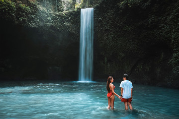 Traveling young couple with tropical rainforest in Bali enjoying life at beautiful Tibumana waterfall.