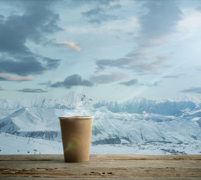 Single tea aor coffee mug and landscape of mountains on background. Cup of hot drink with snowly look and cloudly sky in front of it. Warm in winter day, holidays, travel, New Year and Christmas time.