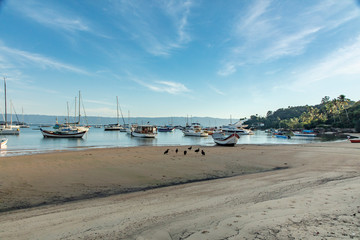 Fototapeta na wymiar Boats in a bay on the coast of Sao Paulo on a beach in Ilhabela island with blue sea and clear sand in Brazil