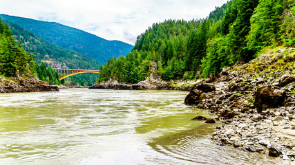 The mighty Fraser River, with the the arch shaped steel structure of the Alexandra Bridge on the Trans Canada Highway in the distance. Viewed from the upstream historic Second Alexandra Bridge
