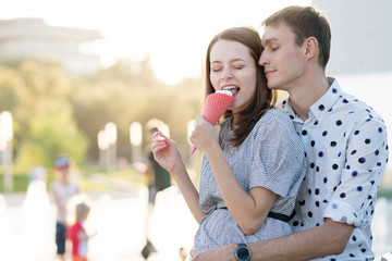 Happy young couple in love having fun and walk on the summer day. Girlfriend and boyfriend spend time together in park. Lovers enjoying themselves prank. Street fast food. Ice-cream and milkshake
