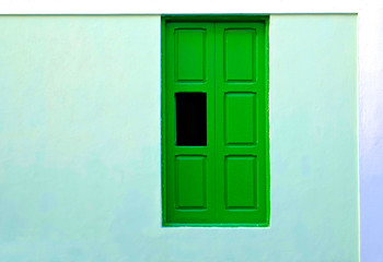 Green shutters in a pale blue wall, with one window panel open, classic villa architecture abstract detail.