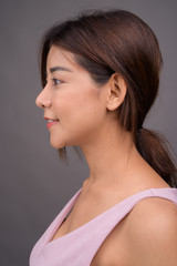 Face of young beautiful Asian woman against gray background