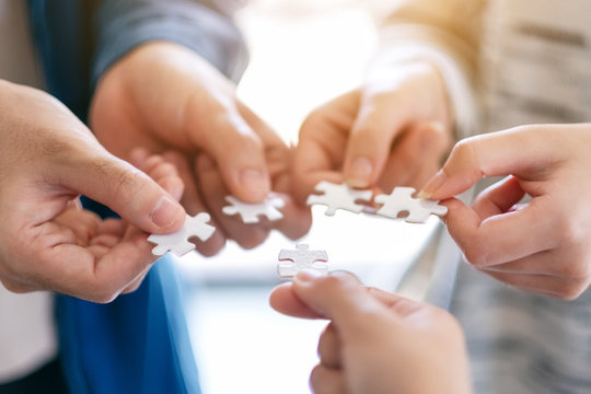 Closeup image of many people holding and putting a piece of white jigsaw puzzle together