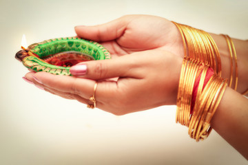 Diwali background content with woman hand holding traditional clay lamp shot with selective focus