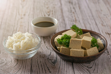 Tofu cheese with soy sauce and rice on a wooden table in the sun.