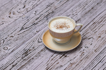 A Cup of fragrant coffee with milk and cinnamon on a wooden table.