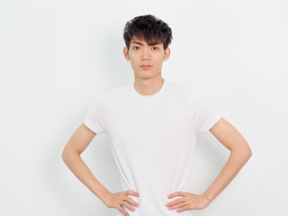 Portrait of handsome Chinese young man in white t shirt posing against white wall background. Two hands on hips with confident expression.