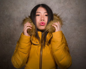 Fototapeta premium young beautiful Asian Chinese woman feeling cold and chilly freezing feeling cold in Winter weather wearing yellow jacket with fur hood isolated on grunge studio background