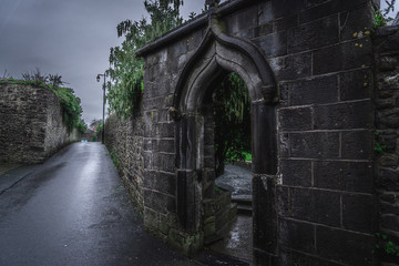 KILKENNY, IRELAND, DECEMBER 23, 2018: Spooky old stone and very wet entrance gate of a graveyard with mold and lichen growing. Concept of desolation and damage.