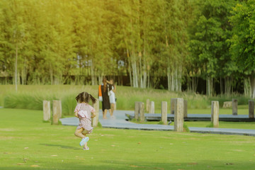 A little girl in a pink skirt enjoys a relaxing time playing on the green lawn at the public park in the evening.