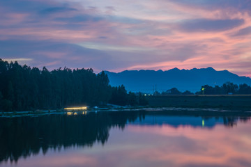 Beautiful view of twilight silhouette sunset on the water reservoir while the sky after sunset has orange light coming out of the clouds and reflecting with the water in the reservoir.