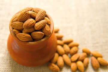 Almond nuts in earthenware on sackcloth background, almonds are unsaturated fats food benefit for decrease blood cholesterol level and good nutrition during diet and lost weight,selective focus