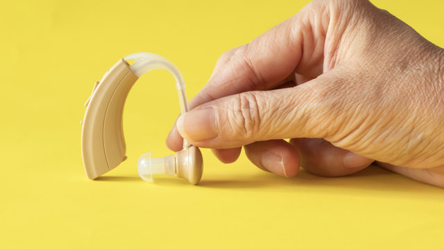 Hand holding hearing aid on yellow background ,high technological treatment device for hearing improvement to  person with hearing loss