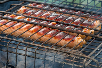 Grilled sausages with smoke and flame on a dark coal background.