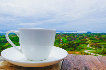 White hot coffee mugs placed on a wooden floor with green fresh mountain and morning fog as background