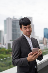 Portrait of young Asian businessman using phone against view of the city