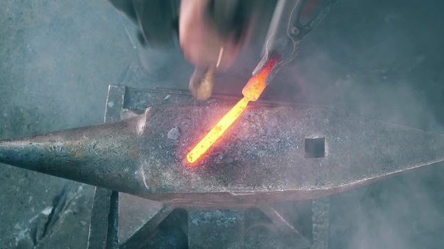 Blacksmith works with knife, hitting it on anvil.