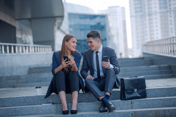 young business couple with smartphones sitting near office building.