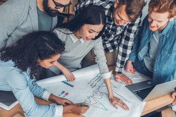 Startupers working together at office standing near table drawing performance graph joyful top view