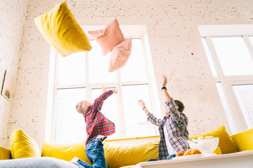Young father with a son, a boy of 8 years in plaid shirts, fighting pillows, happy time together