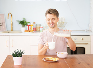 Obraz na płótnie Canvas Happy young blond man having breakfast in the kitchen with milk toast and cereal