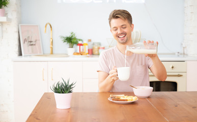 Happy young blond man having breakfast in the kitchen with milk toast and cereal