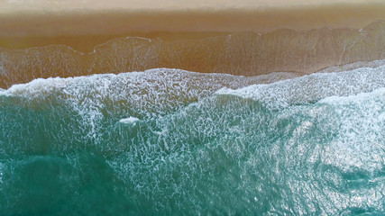 Fototapeta na wymiar Beach on aerial drone top view with ocean waves reaching shore.