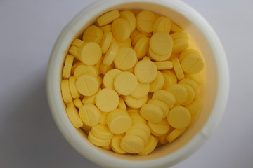 yellow round tablets in white jar in medical healthcare drugstore concept,closed up