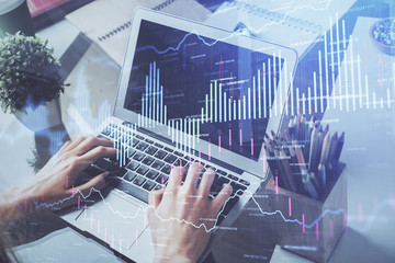 Double exposure of businessman's hands with laptop and stock market graph background. Concept of research and trading.