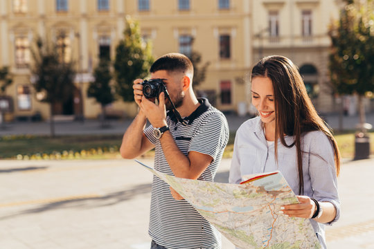 young tourists exploring town using map and taking picture with camera