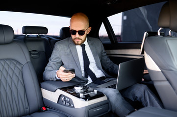 handsome businessman using his mobile phone in a modern car with a driver in center of the city....