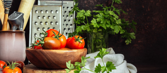 Fresh tomatoes and parsley, dill, garlic on a dark background in a rustic kitchen and wooden utensils still life with copy space