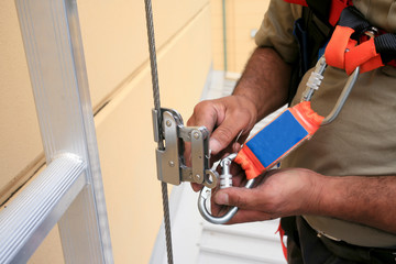 Clipping industrial Karabiner connected with fall arrest shock absorbing safety lanyard device into vertical lifeline steel cable system permanent that run through Aluminium safety ladder construction