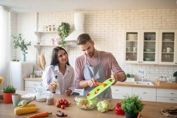 Husband adding some tomatoes to salad while cooking with wife
