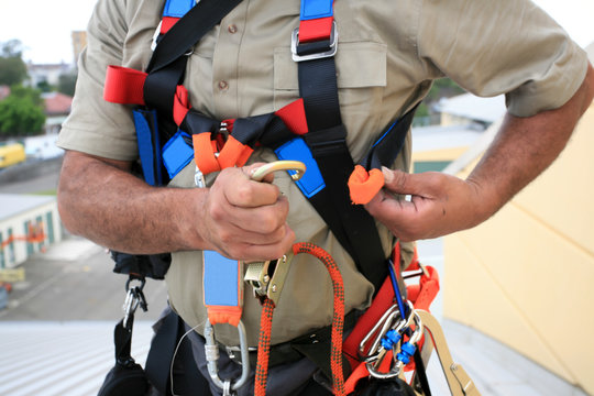 Close up pic of male industrial rope access worker wearing fall arrest, fall restraint safety protection harness clipping Karabiner into side safety harness loop prior work, construction building site