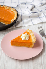 Homemade Thanksgiving pumpkin pie on a pink plate on a white wooden background, low angle view. Close-up.