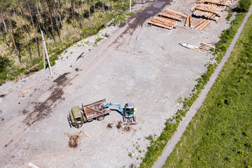 A small blue excavator loads garbage and branches into a truck during cleaning at a construction site or yard. Industrial construction equipment.