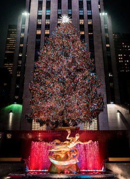 New York, United States, December 25, 2108: A beautiful Christmas tree decorated with colorful lights at night and skyscrapers in the background