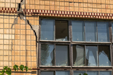 Fototapeta na wymiar Broken windows in an old abandoned brick building. Old windows of ruined abandoned factory with broken windows. Vandalized windows in an abandoned administrative building