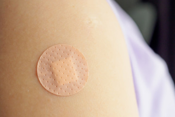 Close up circle brown adhesive bandage on patient arm after medicine injection or vaccination