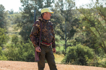 Hunting period, autumn season open. A hunter with a gun in his hands in hunting clothes in the autumn forest in search of a trophy. A man stands with weapons and hunting dogs tracking down the game.	