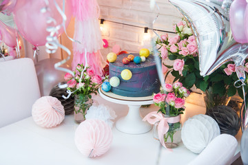 Birthday party blue cake decorated with chocolate balls. Table decorated with balloons, flowers, string lights and paper balls. 