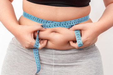 Body Care. Chubby girl with bare belly and tape measure on waist standing isolated on white holding...