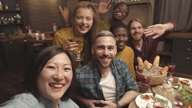 POV shot of happy Asian woman laughing and taking selfie with friends at dinner party in her cozy home