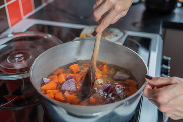  Selective focus of a home cook chef stirring a stainless-steel pan of boiling carrots, ginger, red onion and garlic whilst making a healthy and nutritious homemade soup